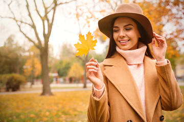 Wall Mural - Young woman in stylish clothes holding yellow leaf outdoors, space for text. Autumn look