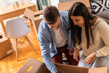 Wall Mural - Smiling young couple move into a new home sitting on floor and unpacking.