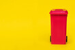 red wheelie waste bin on yellow background.