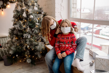 Wall Mural - Young family mother puts a medical mask on her daughter under the christmas tree during home celebration
