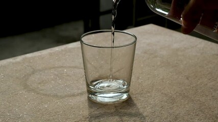 Wall Mural - The drinking water from the bottle is pouring into a clear glass, slow motion.