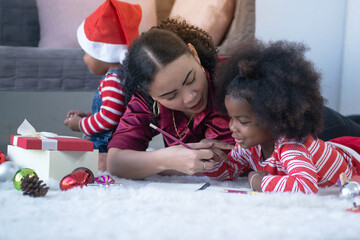 Wall Mural - Dark-skinned girl and her mother lying and playing with her on the floor, her younger brother sitting near her mom, Christmas time