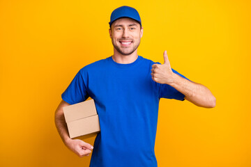 Wall Mural - Photo of positive guy show thumb up arm hold carton package wear hat isolated on yellow color background