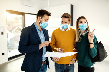 Couple communicating with real estate agent while examining blueprints of a new apartment during COVID-19 pandemic.