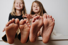 Kids Hold Bare Feet Close Up To The Camera. Their Blurred Giggling Faces In A Background.