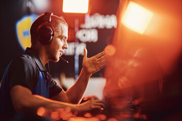 side view of a professional male cybersport gamer wearing headphones talking by microphone with team