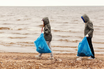 side view of two environmental volunteers, young man and woman in hoods, walking along sea coast and