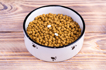 Cat food with two tablets in a bowl on the floor. Vitamins for cats. Treating cats