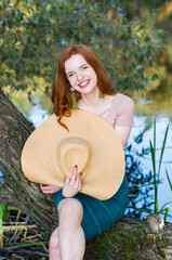 Close up portrait of a beautiful red hair girl in a pink vintage dress and straw hat standing near colorful flowers. Art work of romantic woman .Pretty tenderness model looking at camera.