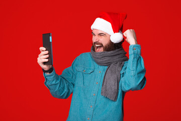 Excited bearded winner wearing christmas hat is looking at his tablet while gesturing.