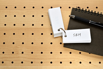 Poster - A notebook and a vocabulary book are placed on the perforated board. The word SEM is written on it.