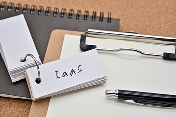 Poster - On top of the notebook and clipboard is a wordbook and pen with the word IaaS written on it. It means Infrastructure as a Service.