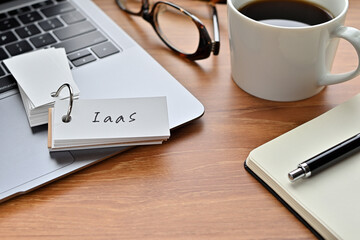 Poster - On a desk with a laptop, glasses, coffee, and a notebook, a vocabulary book was placed open There. The word IaaS is there. It's an acronym that means Infrastructure as a Service.
