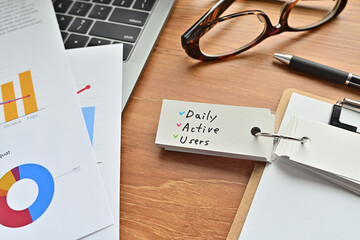 There is a piece of paper with a graph printed on it, a clipboard, and an open vocabulary book on the desk. There is the word Daily Active Users on it.