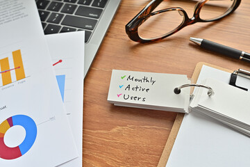 Poster - There is a piece of paper with a graph printed on it, a clipboard, and an open vocabulary book on the desk. There is the word Monthly Active Users on it.