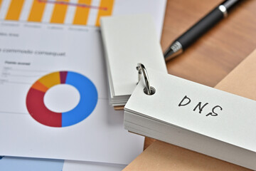 Poster - There is a piece of paper with a graph printed on it, a notebook, and an open vocabulary book on the desk. The word DNS is there. It's an acronym that means Domain Name System.