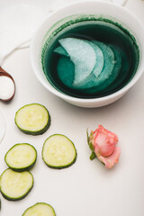 Wall Mural - Tea rose, cucumber slices, bowl with lotion and cotton pads on white surface, stock image