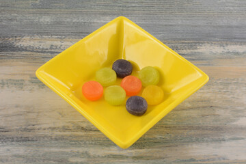 Poster - Round fruit flavored jelly hard candies in yellow candy dish on table