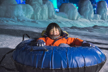 Cute Asian child playing sledge in snow festival on night winter