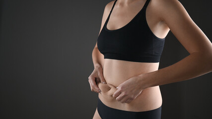 Cropped view of woman in black underwear massaging loose belly with her hands isolated on grey. Skin care and wight loss concept.