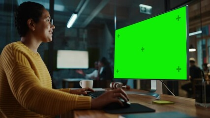 Wall Mural - Young Multiethnic Specialist Working on Desktop Computer with Green Screen Mock Up Display in Creative Office. Beautiful Diverse Female Manager with Short Hair and Glasses is Wearing a Yellow Jumper.