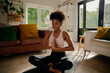 canvas print picture - Young african woman sitting in lotus position with joined hands on yoga mat practicing breathing exercise