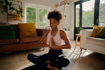 young african woman sitting in lotus position with joined hands on yoga mat practicing breathing exe