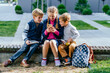 © Iryna - Education, friendship, technology and people concept, back to school. Three different age children sitting outside together. School age older girl play with a cell phone., two boys on the sides.