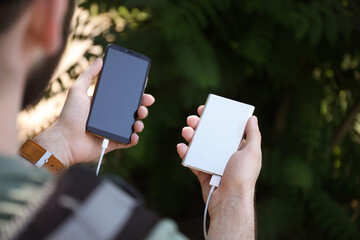 Man charging mobile phone with power bank in forest, closeup