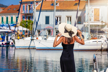 Wall Mural - A tourist woman with hat enjoys the view to the marina of Fiskardo, a little sailors marina at the island of Cephalonia, Greece, during summer time