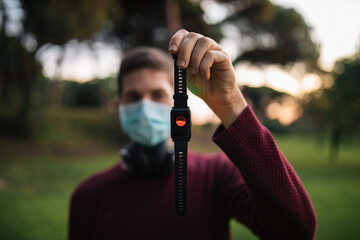 Man with mask holding a smart watch showing the pulses. Concept of healthy living.