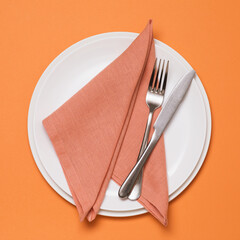 Wall Mural - Rolled up textile napkin in a ceramic plate and cutlery on an orange background, top view