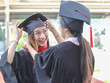 © Phuttharak - cheerful  graduated women in graduation gowns, helping each other dress up, smiling happily. . Education, successful and friendship concept.