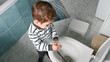 © Tatsiana - Top view of toddler boy in striped clothes washes a toilet. Cute boy in striped clothes washes a toilet. The child cleans at home. Household duties.
