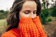 © iuricazac - Closeup portrait of young woman enjoys weather with closed eyes wearing orange knitted sweater posing on nature background. The beautiful female has a dreamy expression, resting outdoors in the park.