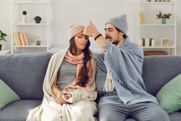 Young man in warm clothes measing body temperature to his sick girlfriend with hand