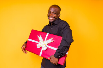 hispanic american man in black t-shirt getting big gift box in studio yellow background