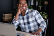 © Rithor - Positive young successful african american designer working on a new project while sitting at a table with a laptop. Handsome smiling mixed race businessman rejoices in career growth