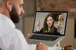 © Roman Tyukin - Back view of a bald male employee with beard who is listening to colleague on a video conference. A laptop screen view of the telecommunications application of an online meeting over a man's shoulder