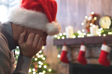 Sad man in Santa Claus hat in a depression feeling negative emotions during christmas celebrations