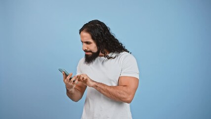 Bearded man networking on smartphone, got message about winning and feeling excited, laughing over blue background.