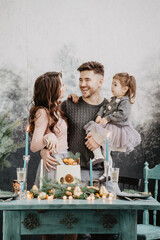 Wall Mural - Young family with a daughter in festive outfits at a served table with candles, garlands, sparklers and a cake near the Christmas tree on New Years Eve