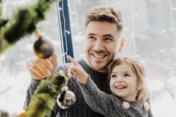 Wall Mural - Father and daughter in festive outfits with a garland near the Christmas tree on New Years Eve