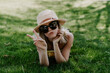 Closeup shot of a beautiful young lady wearing a beach hat and sunglasses lying on the grass