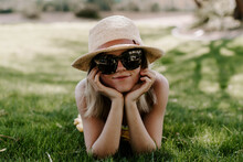 Closeup Shot Of A Beautiful Young Lady Wearing A Beach Hat And Sunglasses Lying On The Grass