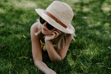 Closeup Shot Of A Beautiful Young Lady Wearing A Beach Hat And Sunglasses Lying On The Grass