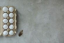Eggs In An Egg Container And A Feather On A Gray Background
