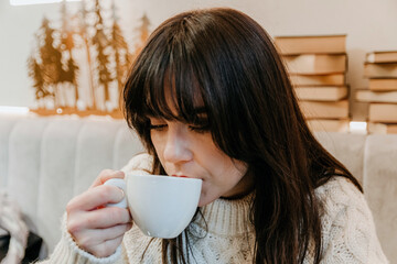 Closeup shot of a young caucasian woman in a warm winter sweater having a cup of coffee in a cafe