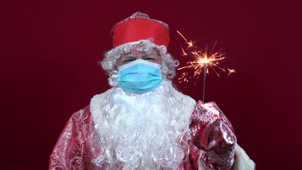 Joyful Russian Santa Claus in a medical mask on a red background holds a Binshgal fire in his hand