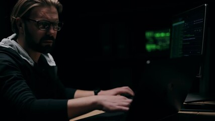 Thoughtful middle-aged man in eyeglasses coding on computer in darkness, innovative technologies, IT